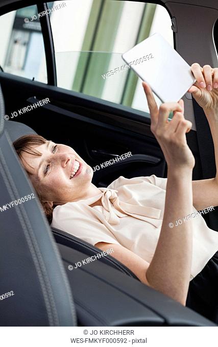 Germany, portrait of smiling businesswoman taking in selfie in her car with digital tablet