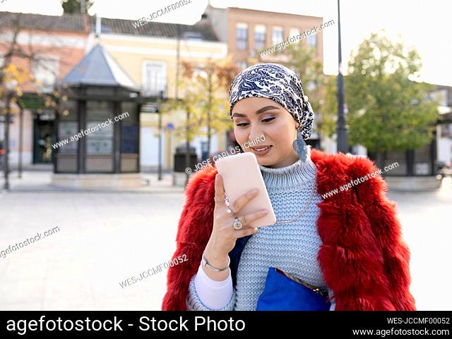 Young woman wearing warm clothing using mobile phone while standing in city
