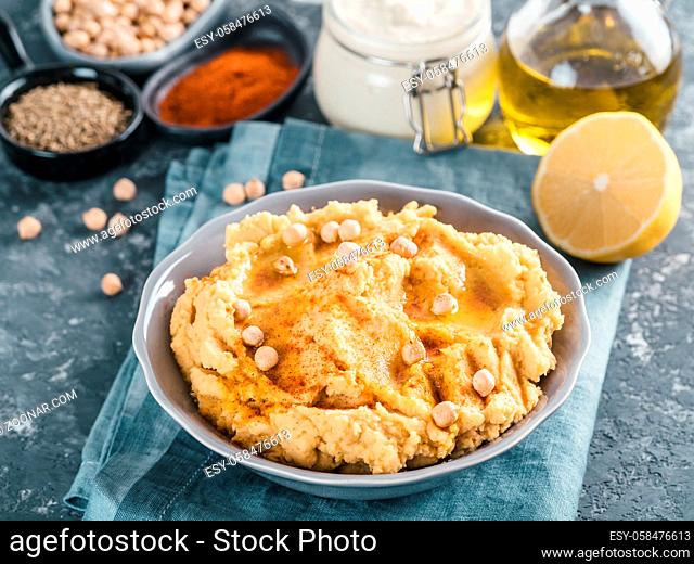Homemade hummus with olive oil in gray bowl and ingredients. Traditional middle eastern appetizer hummus on gray background - healthy vegan paste snack