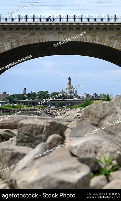 24 July 2023, Saxony, Dresden: Stones of the dried Elbe bank lie below the Albert Bridge in front of the Old Town backdrop with the Frauenkirche and with the...