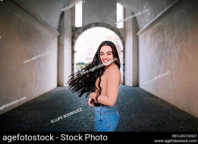 Cheerful teenage girl tossing long hair while standing on footpath in tunnel
