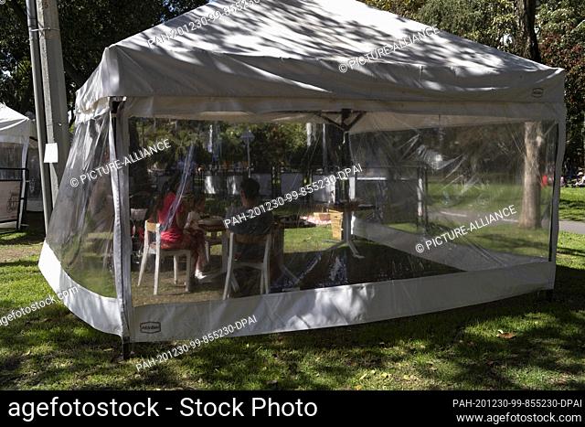20 December 2020, Colombia, Bogotá: A family sits in a pavilion set up next to a restaurant in a park in Bogota. Several restaurants in the city have installed...