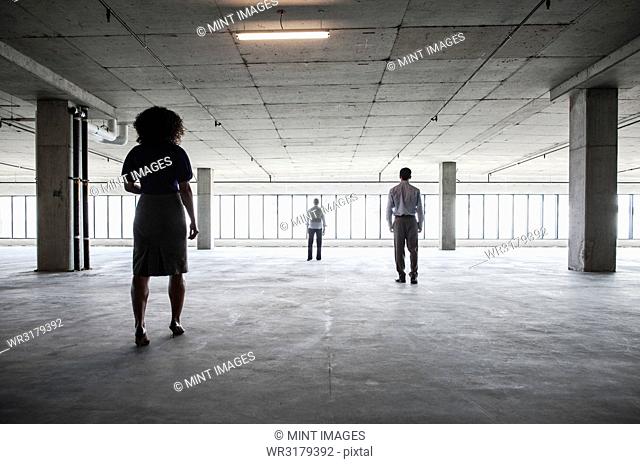 Business people walking toward windows in a large empty office raw space