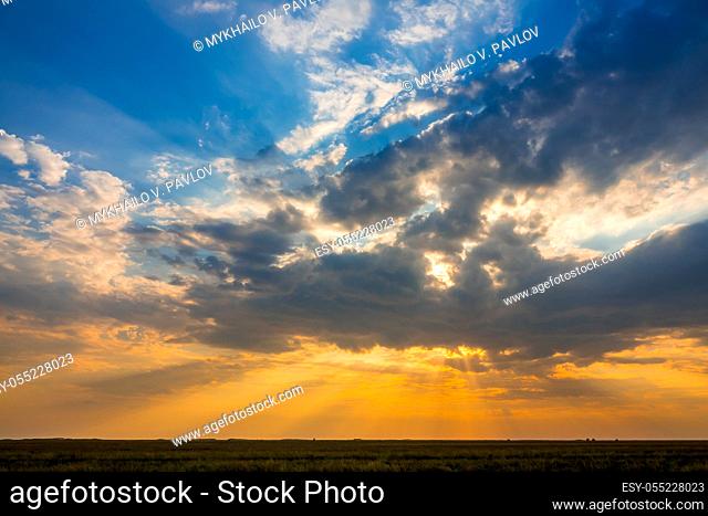 Summer steppe plain. Colorful sunset with many illuminated clouds
