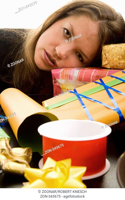 Frau liegt erschöpft mit dem Kopf auf einem Tisch voller Geschenke und Verpackungsmaterial Model: Eva Lux