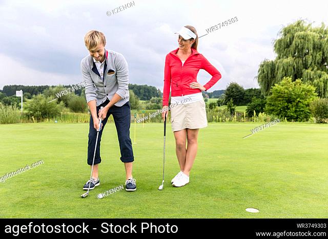Yong female looking at golfer putting golf ball on the green golf