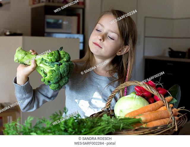 Portrait of girl with wickerbasket of fresh vegetables looking at broccoli