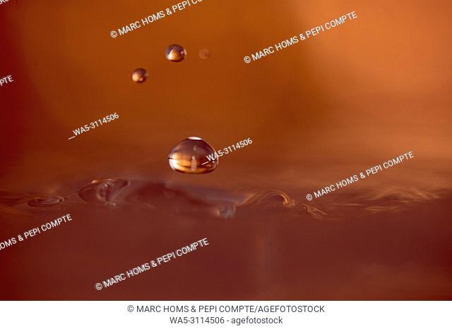 Three drops of copper-colored water suspended above the surface of the water