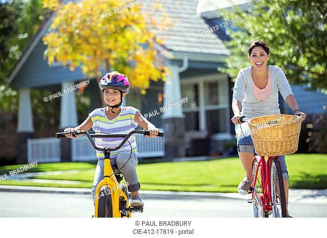 Mother and daughter riding bicycles in sunny street