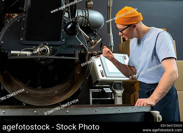 Modern coffee roasting factory, man operating process of creating coffee