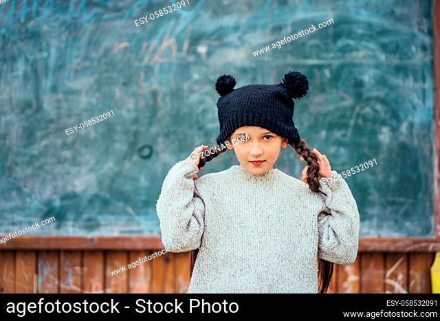 Little girl in autumn park dressed in a jacket and hat stands at the school board