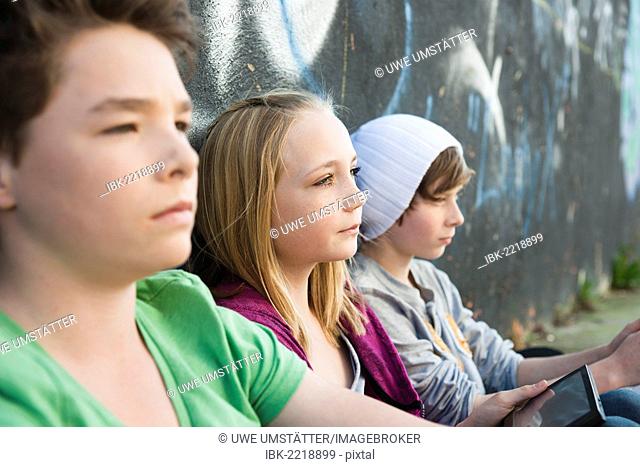 Three teenagers sitting in front of a wall with graffiti