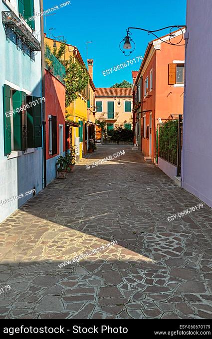 Overview of colorful terraced houses, lamp and bushes in an alley on sunny day in Burano, a gracious little town full of canals, near Venice