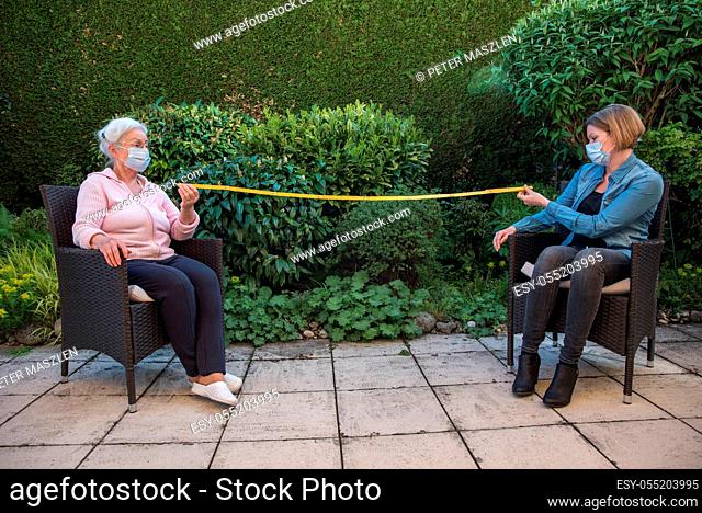 Senior woman and daughter with face masks measuring safety distance
