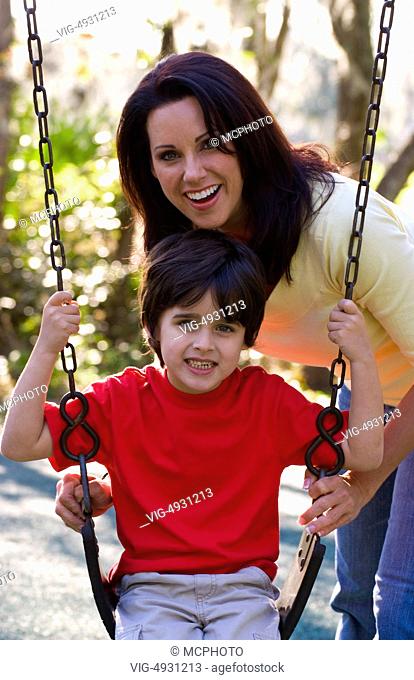 Hispanic mother and son having fun outdoors in park on swing and laughing - 31/03/2020