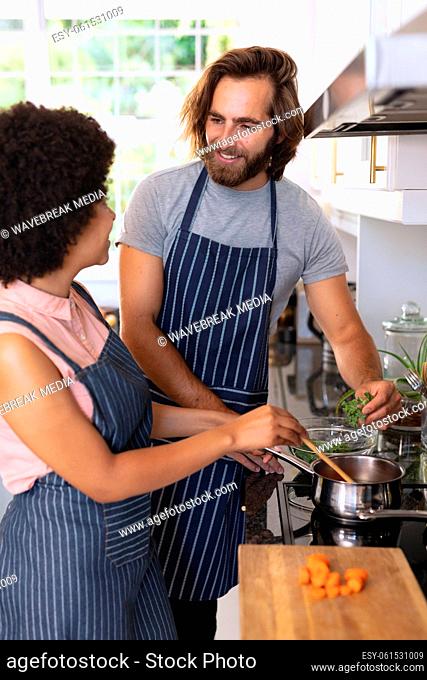 Happy diverse couple in kitchen preparing food and smiling