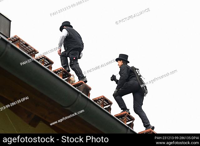 PRODUCTION - 13 December 2023, Bavaria, Munich: Chimney sweep Udo Löbel (l) and his daughter Diane Loebel walk across the roof of a detached house to a chimney