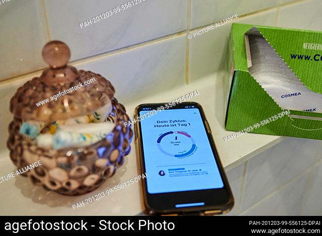 27 November 2020, Berlin: A cycle app on a smartphone is in the bathroom next to panty liners and a jar of tampons. Photo: Annette Riedl/dpa