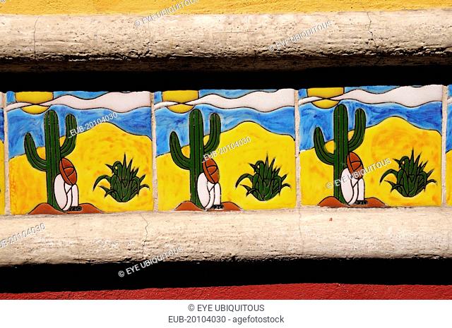 Detail of colourful tile depicting figure in Mexican hat sitting at foot of cactus