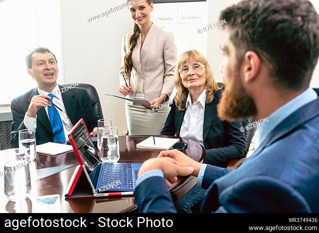 Happy middle-aged managers listening to their younger colleague while planning business in the conference room of a successful corporation