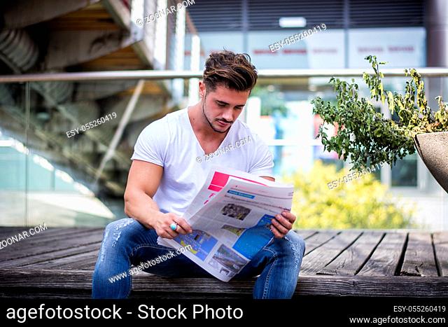 Handsome man reading newspaper outdoor in city setting, sitting on steps