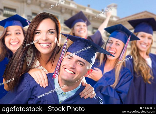 Proud male graduate in cap and gown with girl among other graduates behind