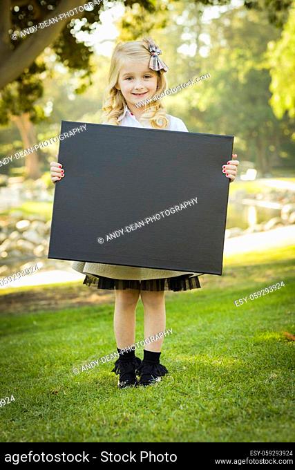 Cute Little Blonde Girl with a Bow in Her Hair Holding a Black Chalkboard Outdoors.