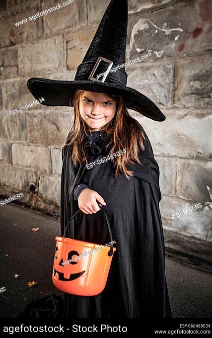 Young girl dressed in a witch costume with tall black hat and holding a pumpkin pail for halloween