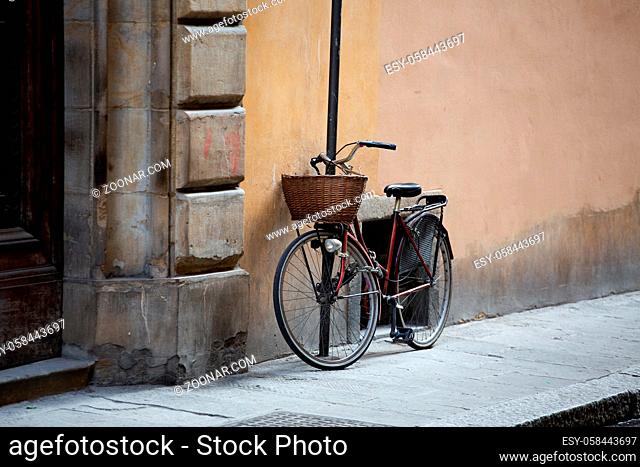 Bicycle standing near wall of ancient building. Female bike with wicker basket in front is fastened with chain to post on street of European city