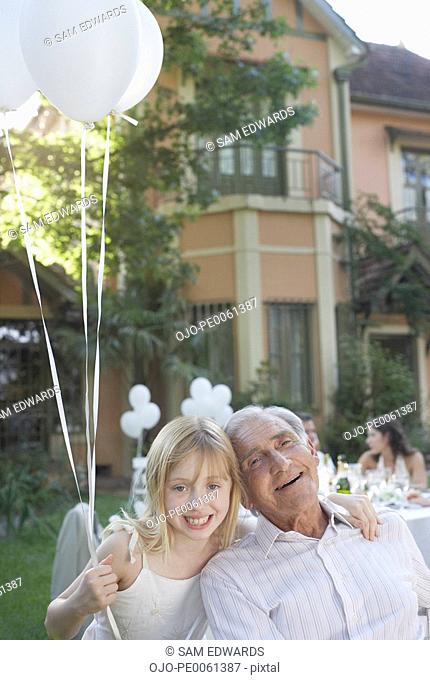 Senior man at outdoor party with young girl holding balloons and smiling