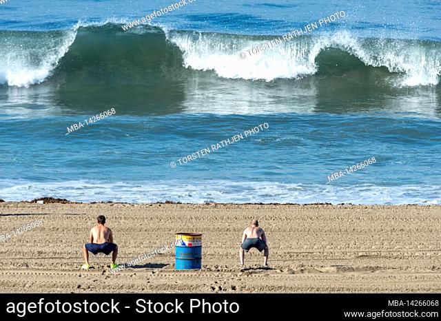 2 athletes doing gymnastics in front of big waves, Santa Monica, California