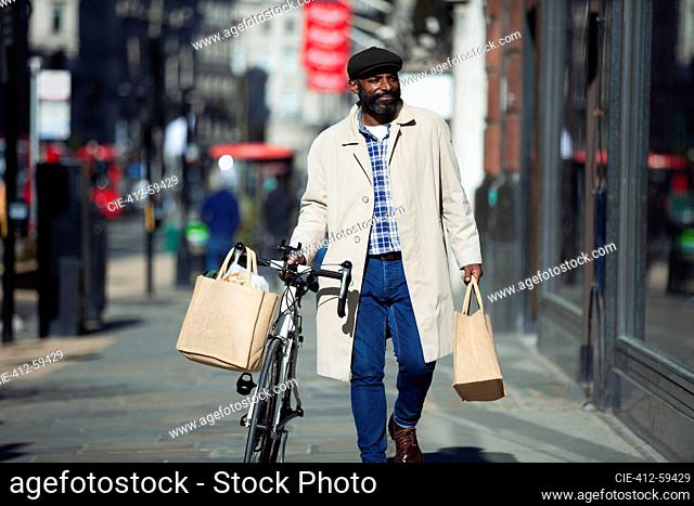 Man with bicycle and grocery bags walking in sunny city