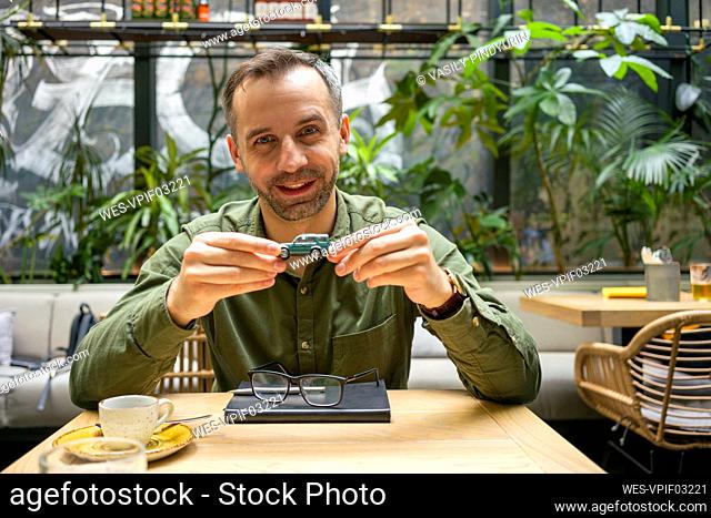 Confident businessman holding toy car while sitting at cafe