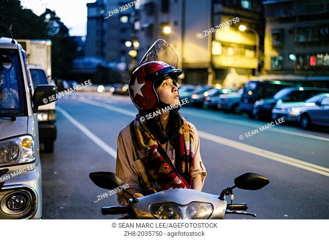 A girl on her scooter looks up into the evening sky in Taipei, Taiwan