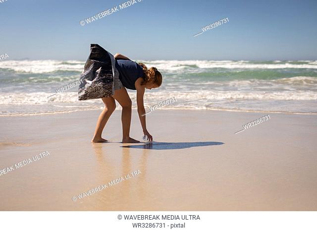 Side view of young Caucasian female volunteer cleaning beach on a sunny day. She is touching the sand
