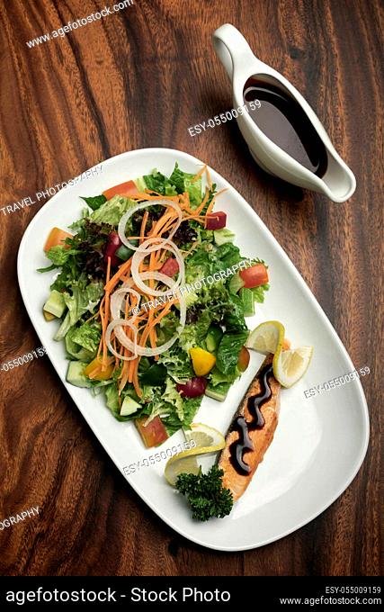organic mixed vegetable salad with salmon fillet and balsamic vinaigrette on wood restaurant table