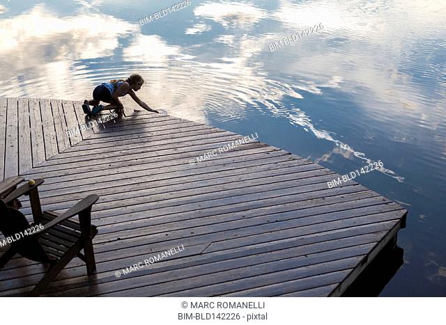 Caucasian girl on wooden deck making ripples in lake