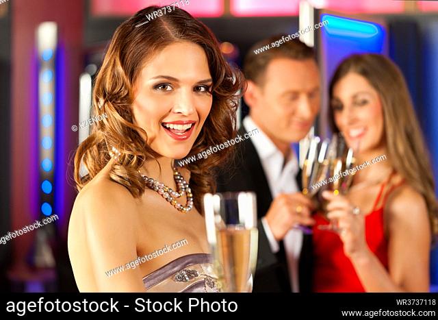 Three friends with champagne in a bar or casino, a woman is looking in the camera