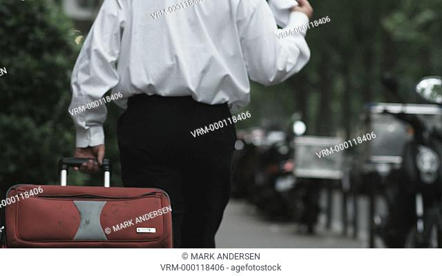 businessman walking down a city street in Europe dragging a suitcase and looking at a map