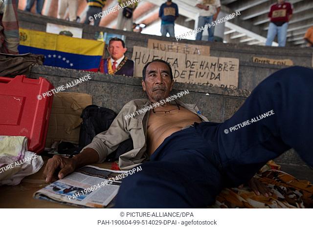 04 June 2019, Venezuela, Caracas: A man lies in front of a Venezuelan flag and a portrait of the late head of state Hugo Chavez in a protest in which former oil...