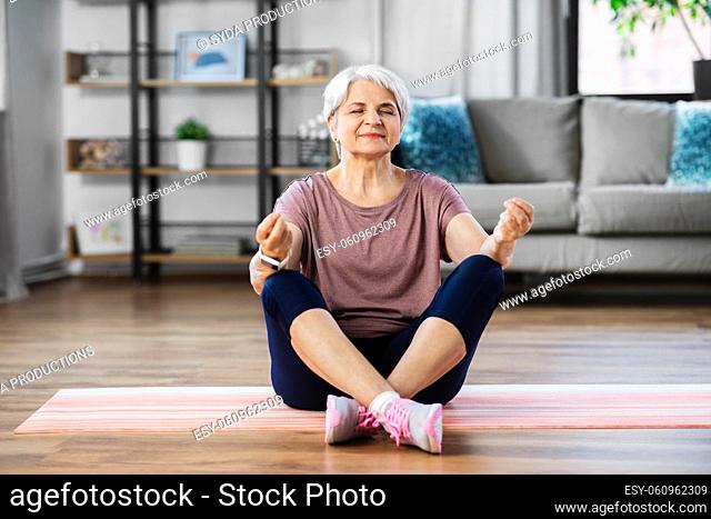 happy senior woman meditating on mat at home