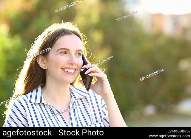 Happy woman talking on cell phone walking in a park