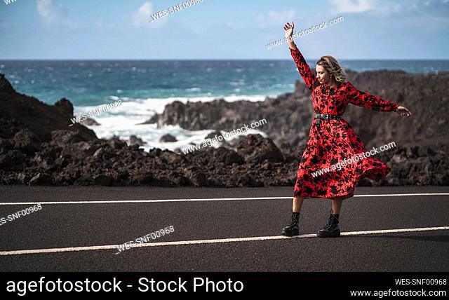 Woman with hand raised dancing while standing on road at Los Hervideros, Lanzarote, Spain