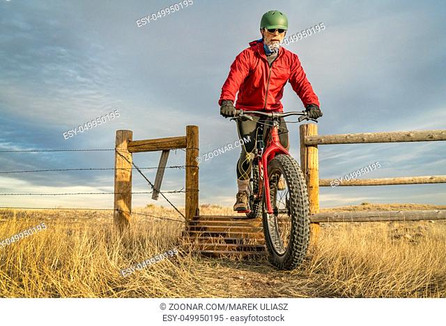 a senior male is riding a mountain fat bike over a cattle guard in Soapstone Prairie Natural Area in northern Colorado, late fall scenery