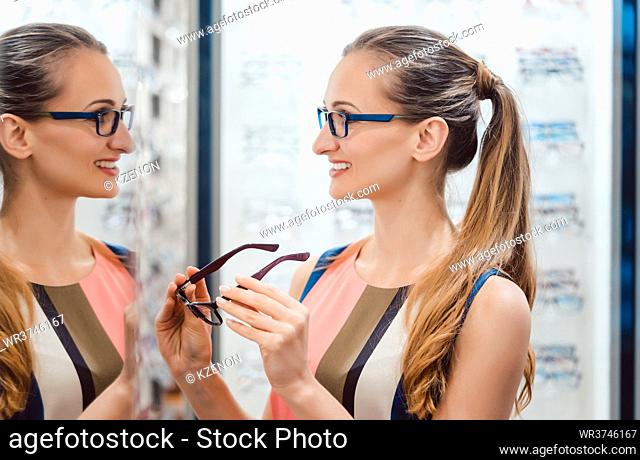 Young woman in optometrists store checking her looks with the new glasses in mirror