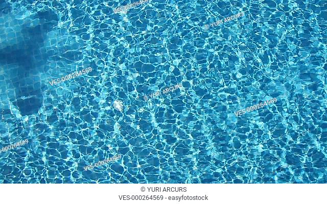 Top view of a woman swimming breast stroke across a bright blue pool from left to right