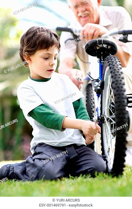 Portrait of sweet little child fixing his bicycle tyre with grandfather at the park