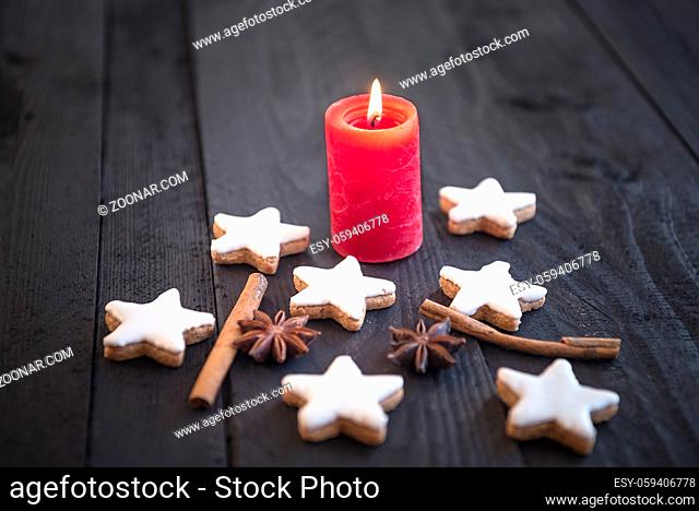 Winter traditional cinnamon and nuts cookies, homemade, star shaped, with decorative spices among them, under candlelight, on an old wooden table
