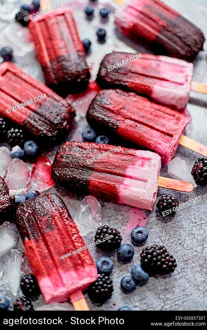 Homemade blackberry and cream ice-creams or popsicles with frozen berries on black slate tray over dark grunge backdrop. Top view, flat lay