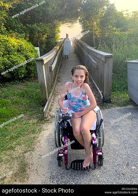 Girl with Ullrich Congenital Muscular Dystrophy sits in her bathing suit in a wheelchair on a path to the beach after a swim in the Pamlico Sound; Nags Head